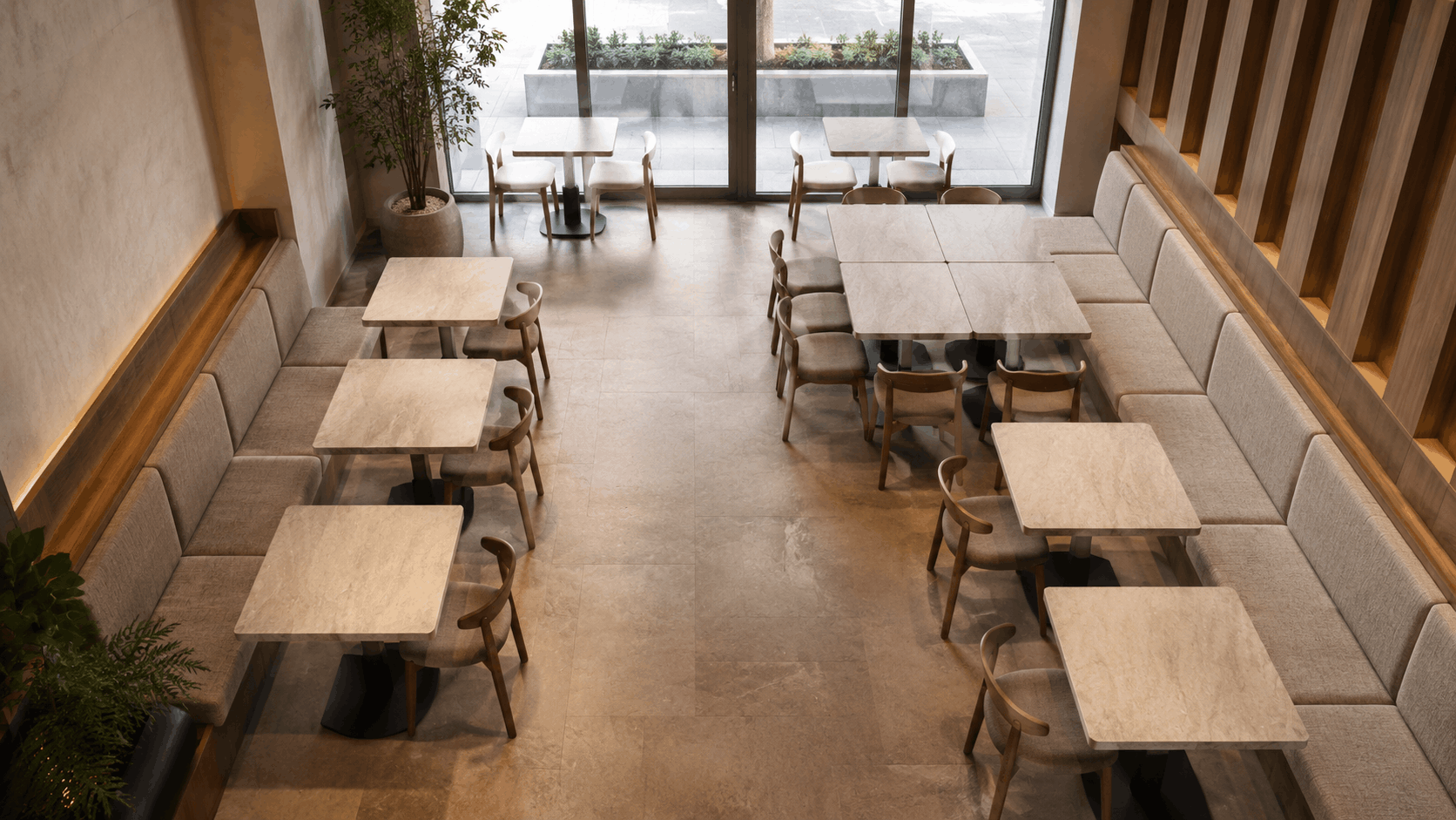 Overhead view of a café with stone-top tables, curved wood chairs, and upholstered banquette seating along both walls